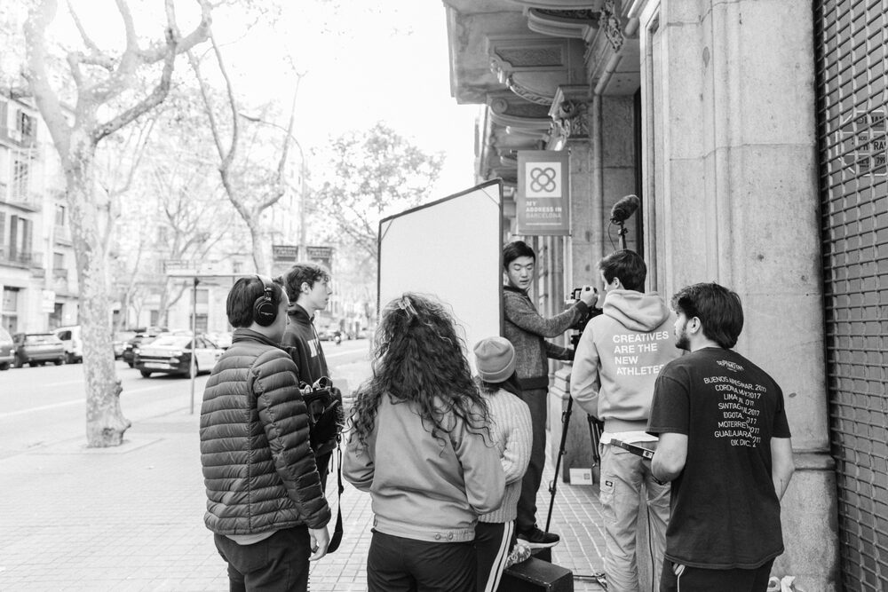 Film crew gathered on a tree-lined sidewalk with a bounce board