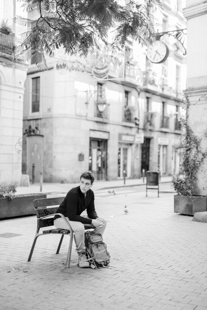 Black and white photo of a man seated on a chair in a courtyard