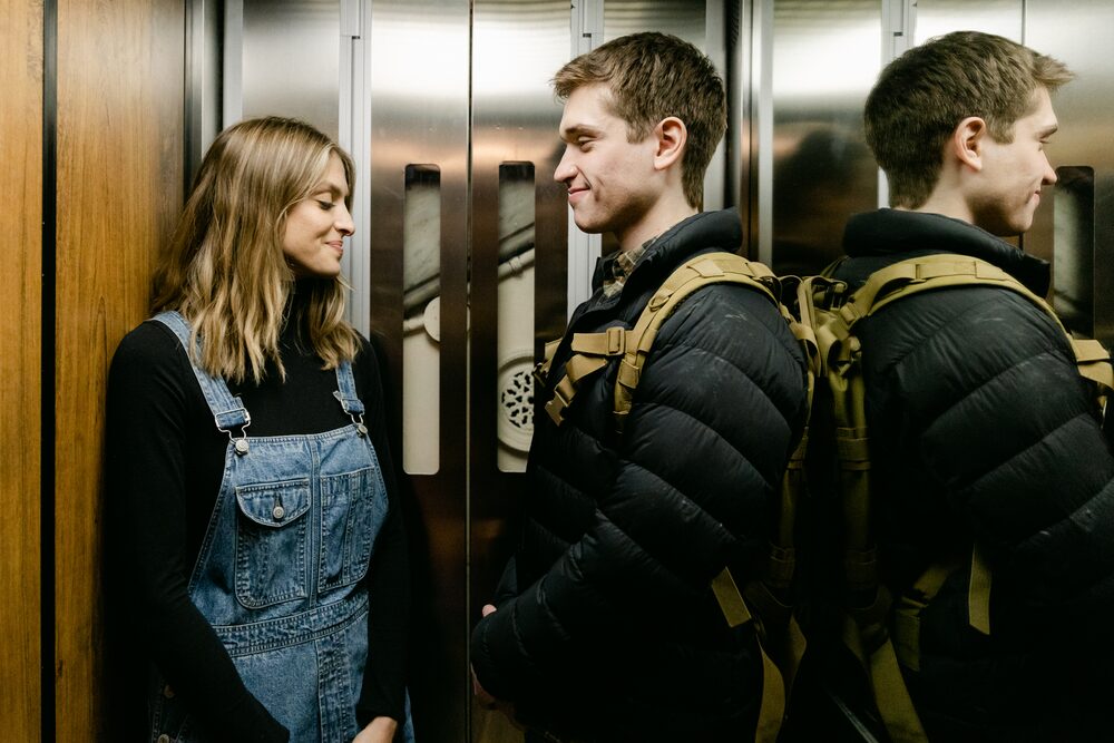Two actors in an elevator, one in overalls
