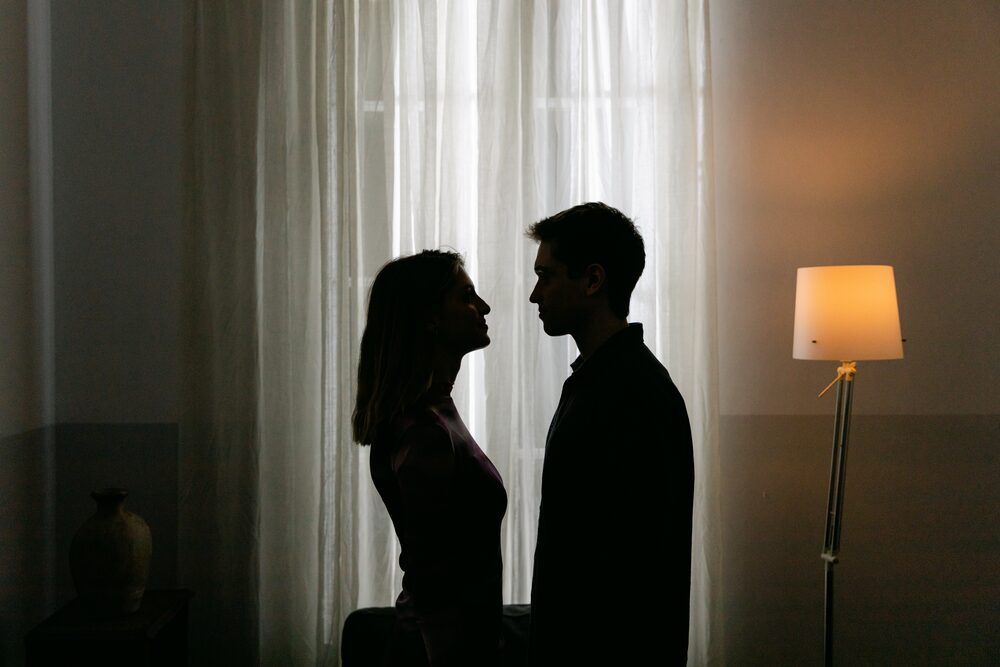 Silhouetted couple facing each other beside a floor lamp