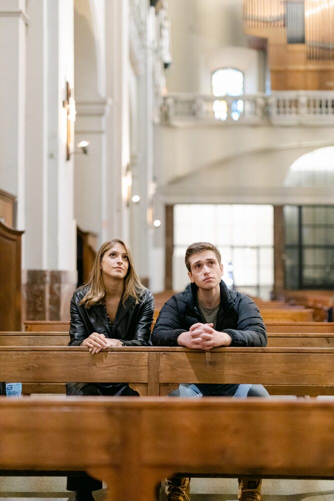 Two actors seated in a wooden church pew