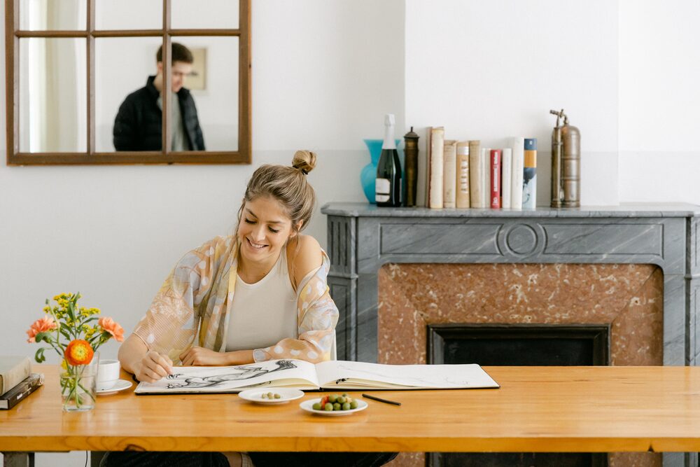 Woman working at a wooden table by a marble fireplace