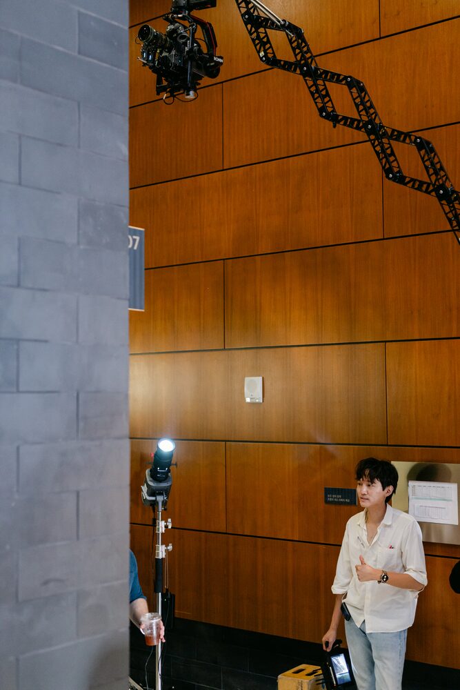 Actor waiting beside a wood-panelled wall under a stand light