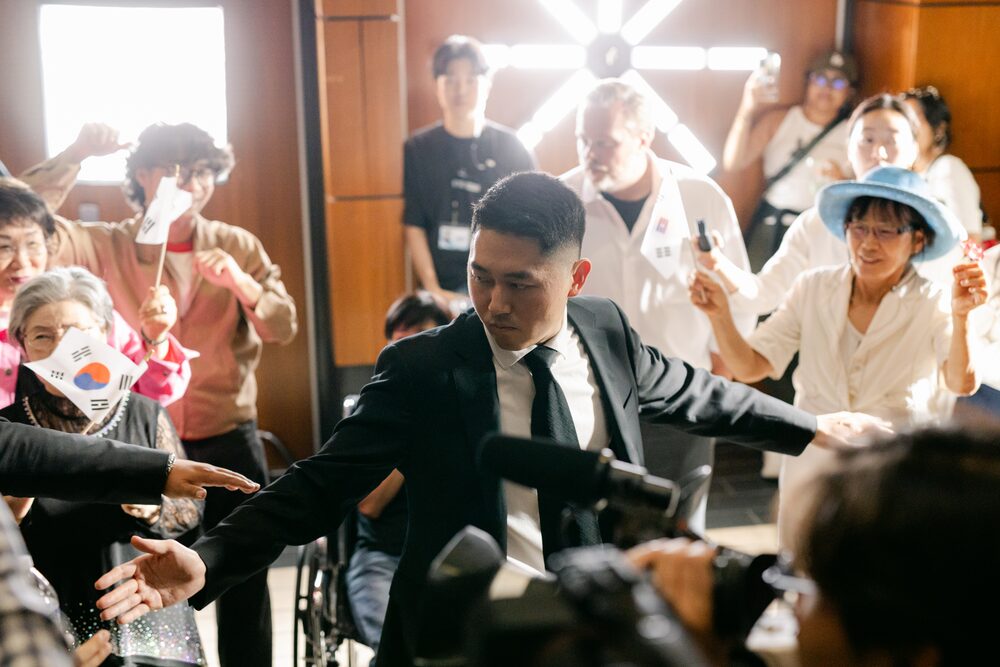 Actors in suits moving through a crowd on a staircase