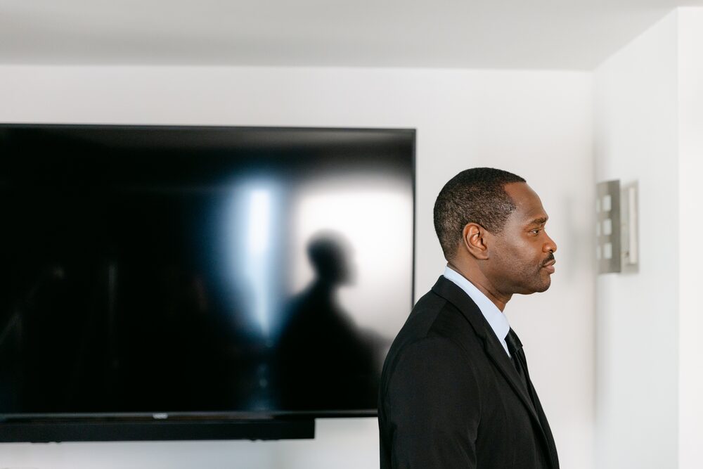 Man in a suit in profile beside a wall-mounted screen