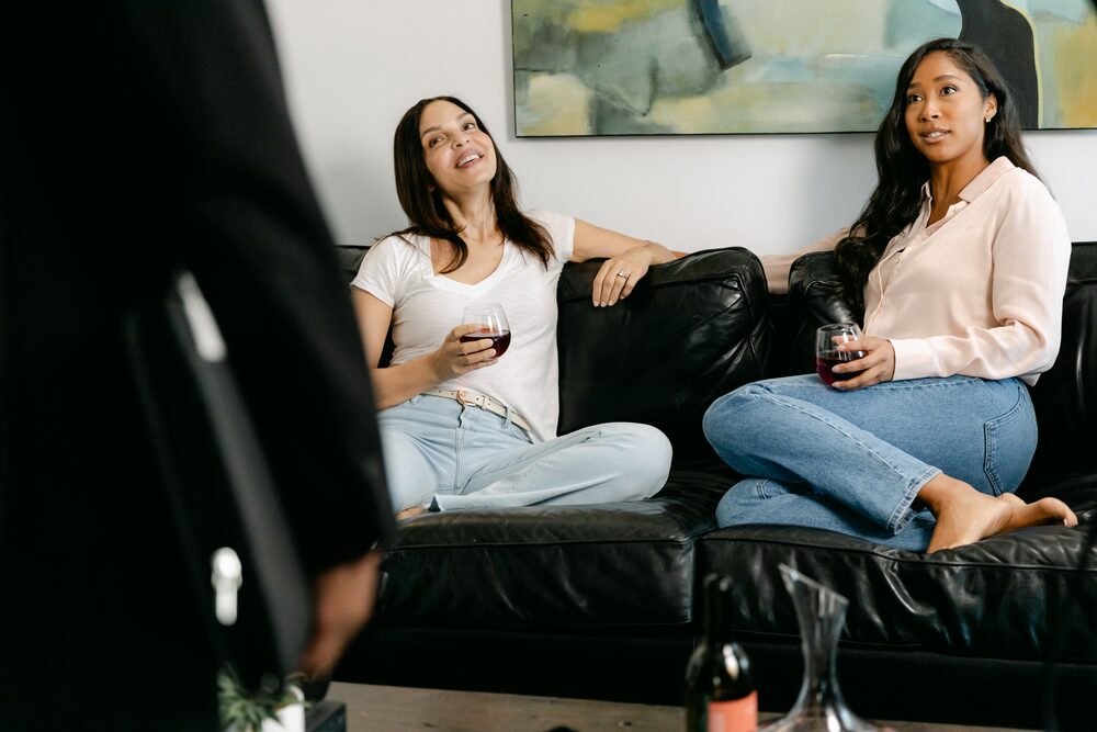 Two women laughing on a black leather sofa