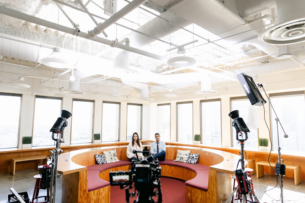 Film lights set up in a sunlit lounge with a curved sofa