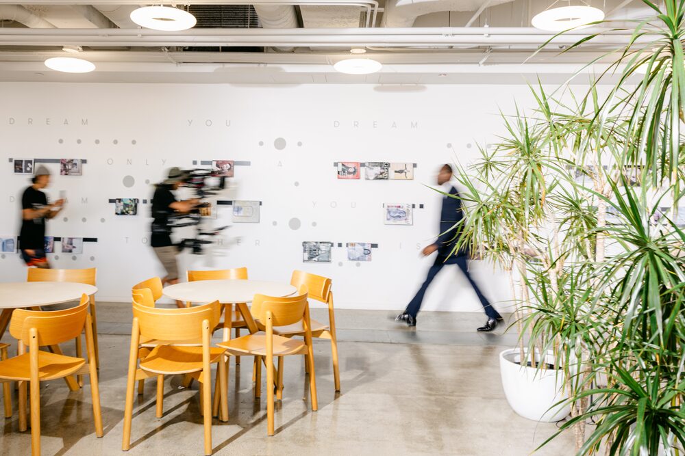 Person walking through a café with wooden chairs and plants