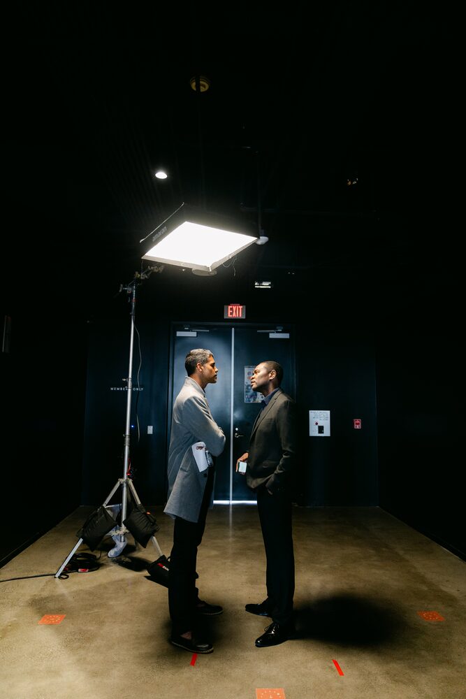 Two actors under a single softbox light in a dark studio